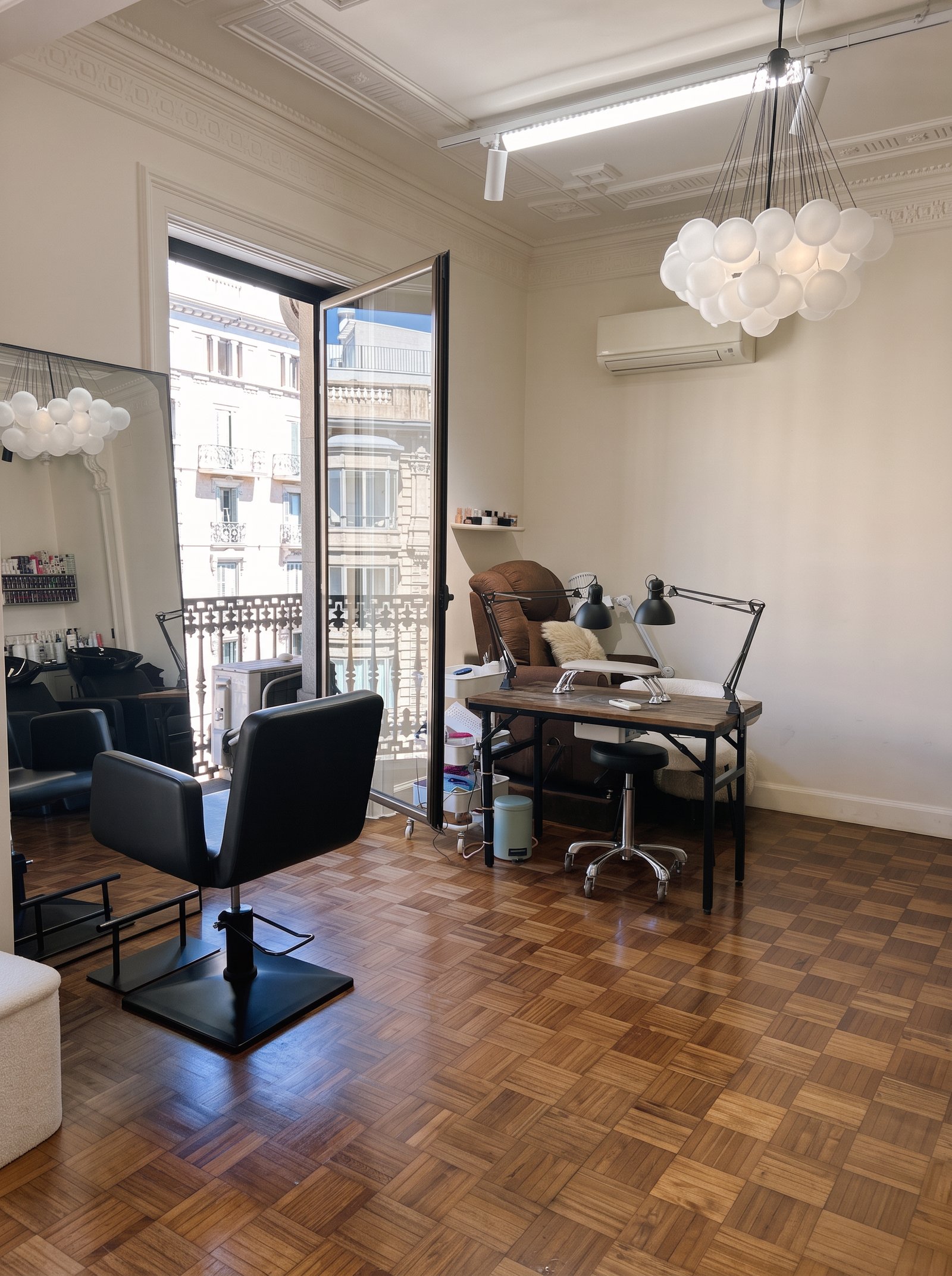 Sala de Couture con sus sillones, el parquet de espiga y la lámpara de esferas frente al balcón